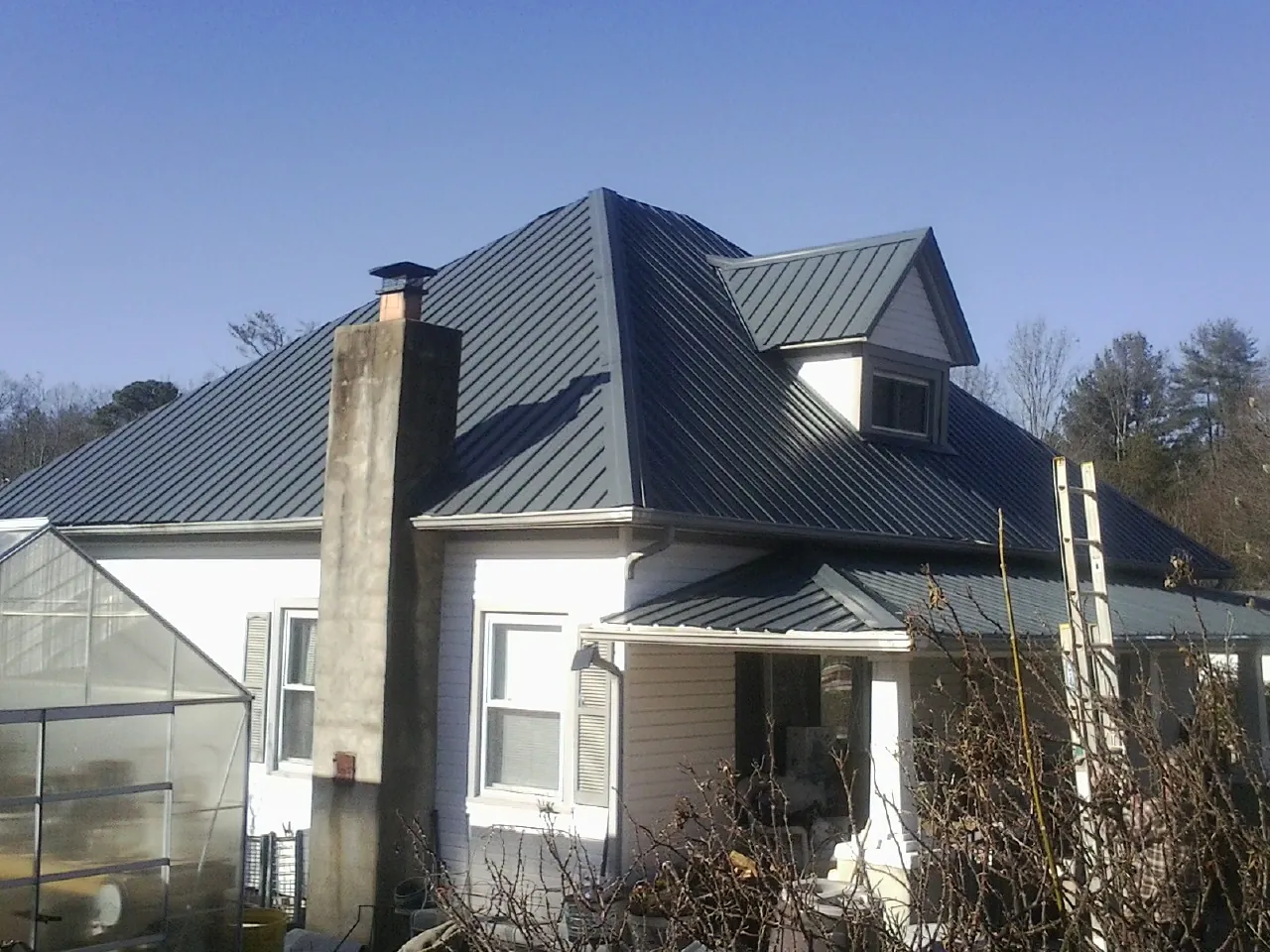 Dark blue standing seam metal roof on a white farmhouse with dormer — Slate & Tile Roof Repair by Roofing Brothers in Jacobsburg