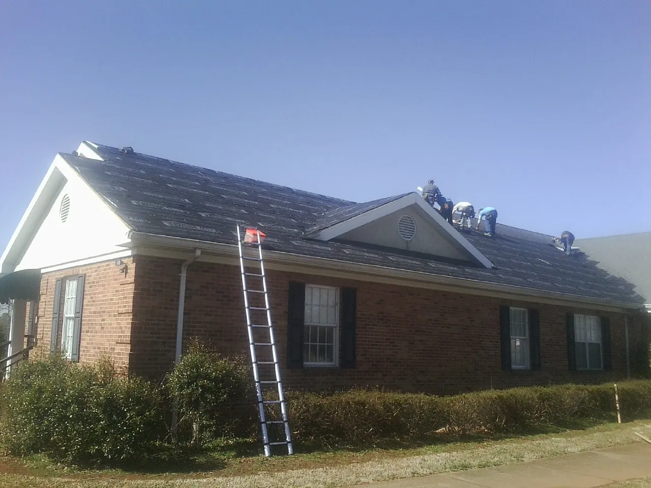 Crew tearing shingles off a brick ranch roof with a ladder set — Emergency Roof Repair work by our crew in Jacobsburg