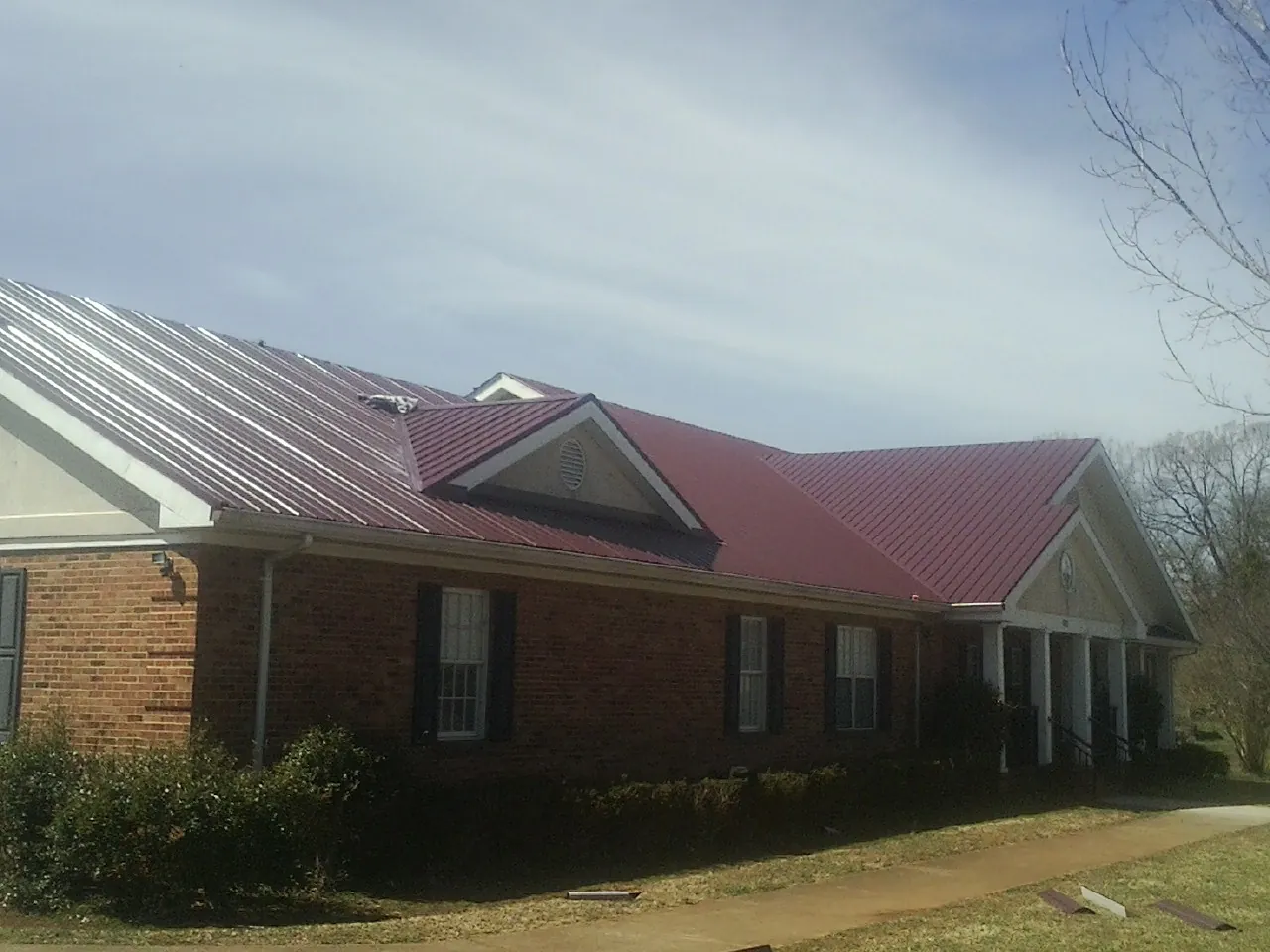 Red metal roof with gabled entries on a long brick building, from a Hail Damage Roof Repair job in Jacobsburg