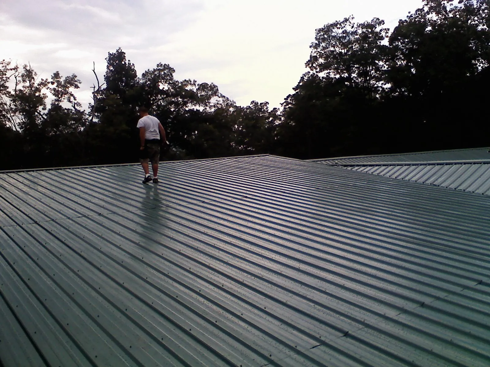 Roofer walking a wide expanse of new green metal roofing in Jacobsburg