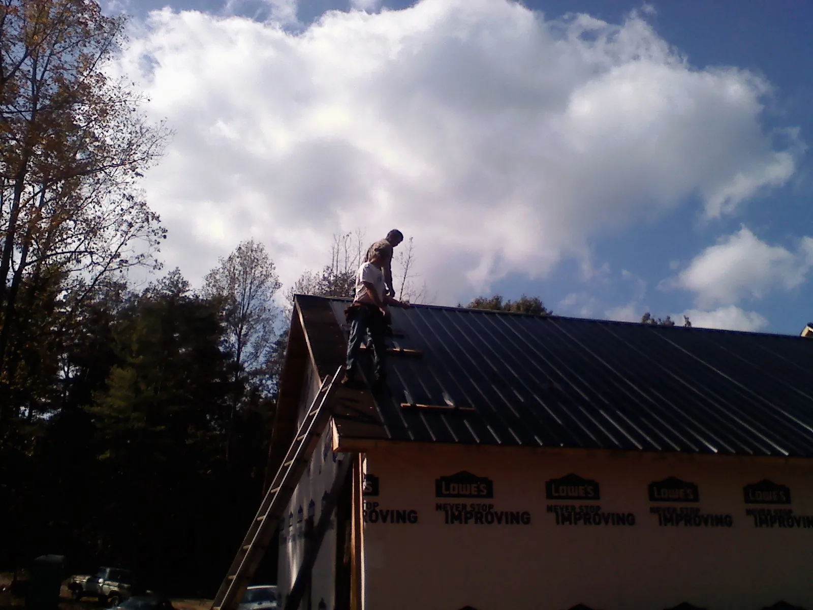 Roofer fastening dark metal panels high against a cloudy sky, from a Roof Inspection job in Jacobsburg