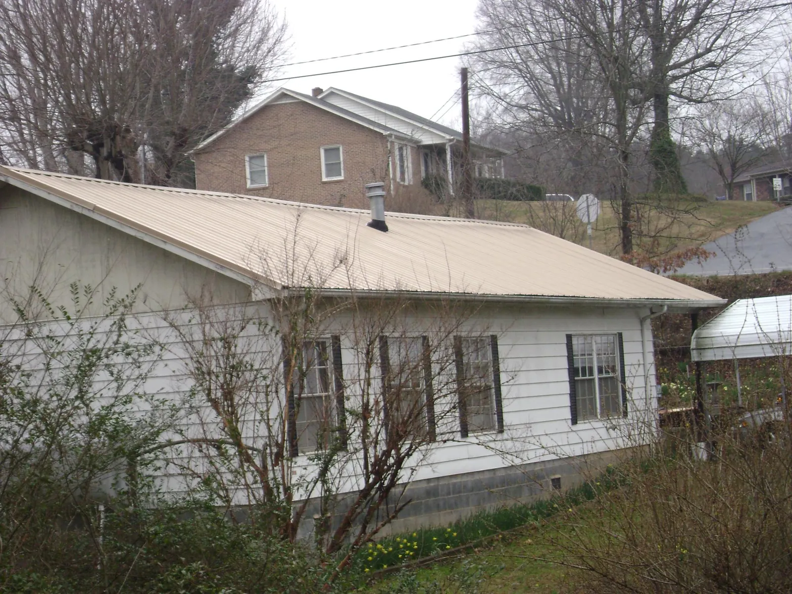 Tan metal roof on a white sided house set into a hillside — Commercial Roofing by Roofing Brothers in Jacobsburg