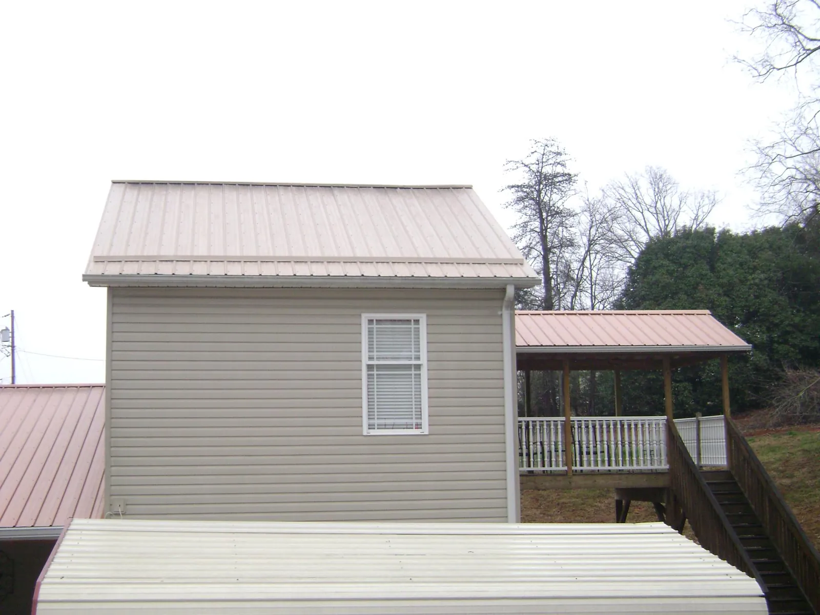 Tan metal roofs on a two story addition and attached porch, from a Roof Replacement job in Jacobsburg
